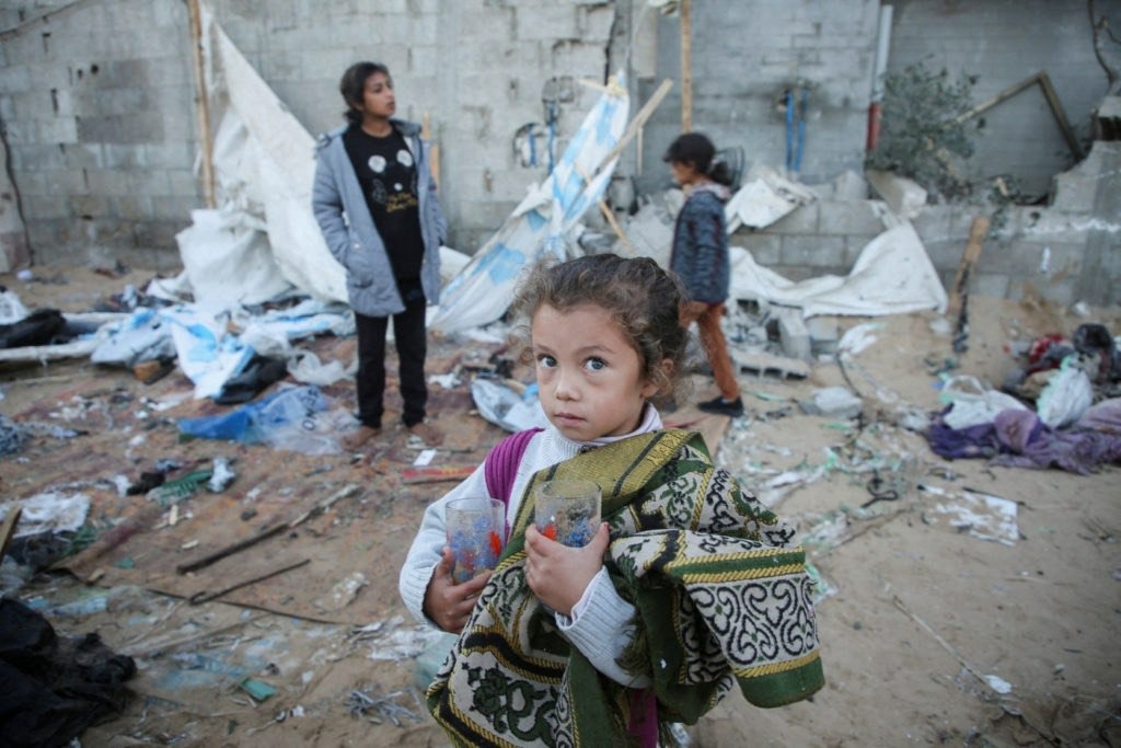 A young girl holding glass cups standing amidst complete rubble