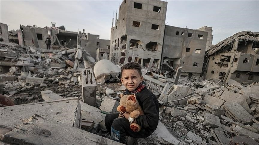 Young child sitting in rubble holding a stuffed animal